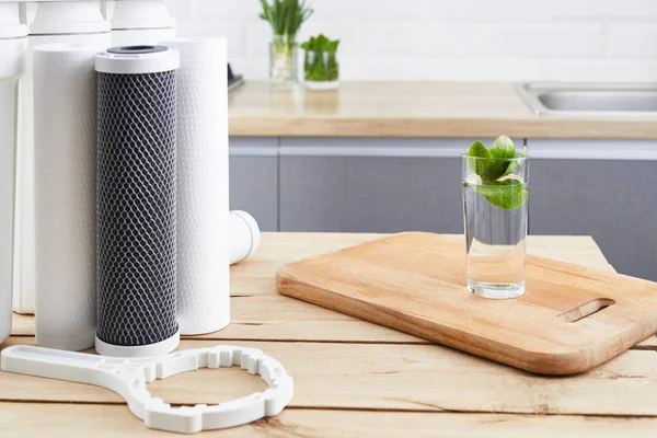 A glass of clean water with osmosis filter and cartridge on wooden table in a kitchen . Concept filtration system. — Stock Photo, Image