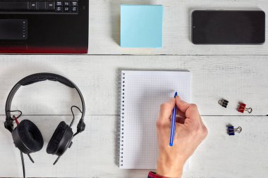 Man's hand writing in notebook on white wooden table. Working place and planning concept, top view.