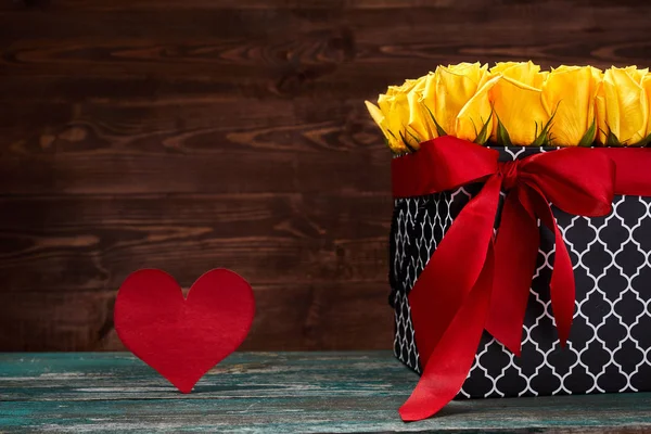 木製の背景に赤い紙の心を持つ紙箱の黄色いバラ。バレンタインデーのコンセプト. — ストック写真