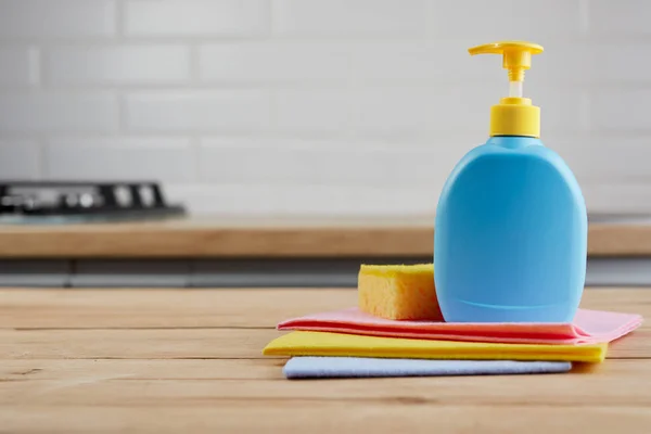 Esponja amarilla y botella de plástico azul en mesa de madera con paños de color, fondo de cocina — Foto de Stock