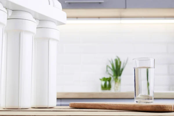 Un bicchiere di acqua pulita con filtro osmosi su tavolo in legno in cucina — Foto Stock