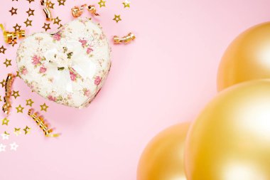 Heart shaped Valentines Day gift box on pink paper background. holiday background with , gold curved ribbon and Balloon.
