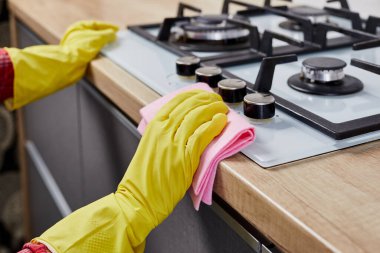Koruyucu eldivenli bir kadın gaz sobasını paçavrayla temizliyor. Kapat.