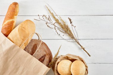 Ekoloji kese kağıdında tam tahıllı ekmek, beyaz ahşap arka planda. En üstteki düz yerde. Sağlıklı yiyecekler. Ekoloji kavramını sakla. Sıfır atık geri dönüşümü