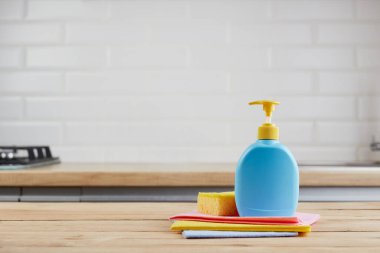 sarı sünger ve mavi plastik şişe, ahşap masa üzerinde sıvı sabun, renk bezleri, mutfak arka planı, kapat.