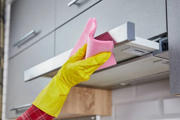 Woman Cleaning Cooker Hood With Rag In Kitchen. Close up of female hand in rubber protective yellow gloves clean the kitchen metal extractor hood with rag. housekeeping concept