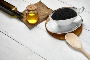 Masadaki seramik kasede siyah kimyon tohumu cam kavanozda ve şişede soğuk ezilmiş yağ..