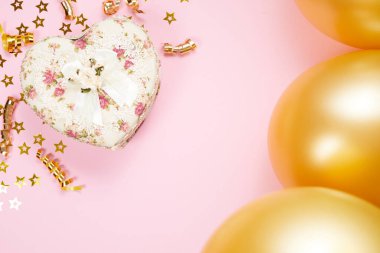 Kalp şeklinde Sevgililer Günü hediye paketi pembe kağıt arka planda. Küçük yıldızlı, altın kıvrımlı kurdeleli ve balonlu güzel bir tatil geçmişi var..