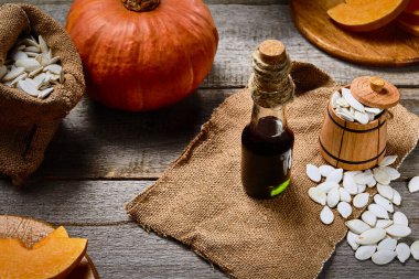 Cam şişede soğuk baskılı balkabağı tohumu yağı, çuval bezinde tohumlarla süslenmiş çiğ pampkin ve küçük ahşap fıçı.