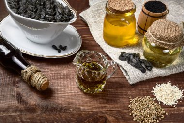 Ayçiçekli şişeler, siyah kimyon, kenevir ve susam yağı ve tohumlar ahşap bir arka planda