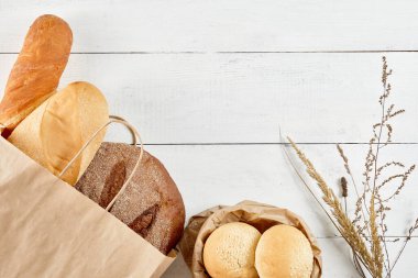 Ekoloji kese kağıdında tam tahıllı ekmek, beyaz ahşap arka planda. En üstteki düz yerde. Sağlıklı yiyecekler. Ekoloji kavramını sakla. Sıfır atık geri dönüşümü