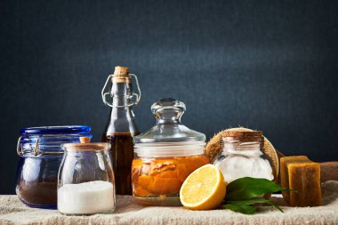 Eco-friendly natural cleaners: baking soda, soap, vinegar, salt, coffee, lemon and brush on a wooden table. Dark background.