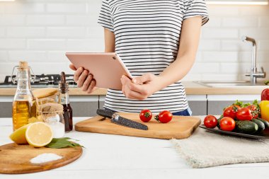 Kadın mutfakta duruyor ve salatayı pişiriyor. Tablet bilgisayarına bakılıyor.