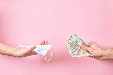 Medical mask and dollars in hand as a concept of increased prices for protecting from viruses.