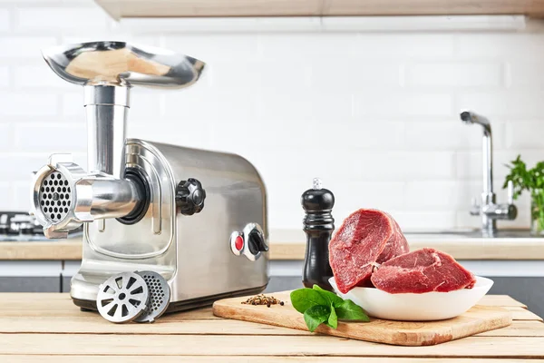 Meat grinder with fresh meat on a wooden table in kitchen interior