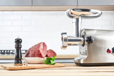 Meat grinder with fresh meat on a wooden table in kitchen interior clipart
