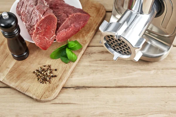 Meat grinder with fresh meat on a wooden table in kitchen.