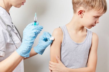 Genç bayan çocuk doktoru küçük bir çocuğa aşı yapıyor.