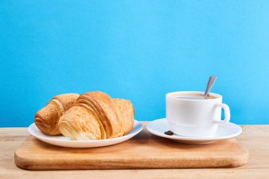 Kruvasanlarla kahvaltı. Taze kızarmış kruvasanlar ve mavi arka planda kahve ve ahşap masa.