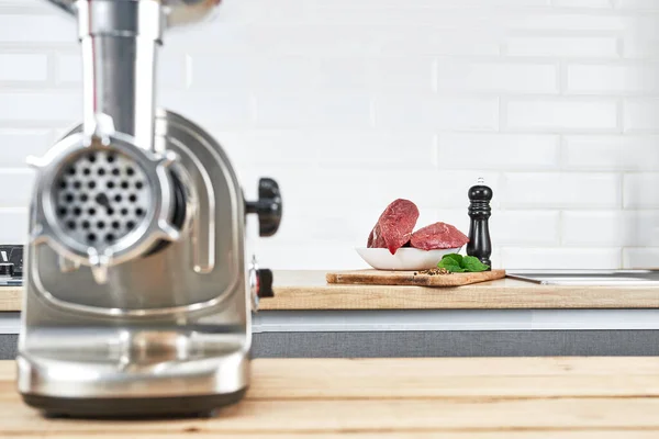 М'ясорубка зі свіжим м'ясом на дерев'яному столі в інтер'єрі кухні — стокове фото