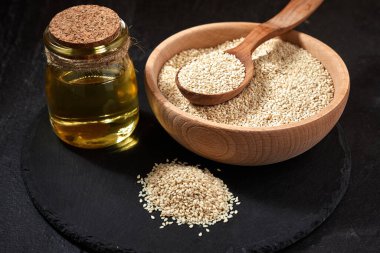 Susam tohumları ve karanlık bir masada tahta bir kaşık. Ahşap kase ve bir şişe yağlı siyah levha. Uzayı kopyala Kapat.