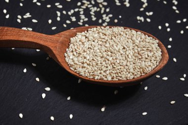 Karanlık bir masada susam tohumu ve tahta bir kaşık. Sağlıklı yiyecek ve içecek konsepti. Üst Manzara. Kapat.