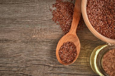 Tahta bir masada keten tohumu ve tahta bir kaşık. Bir şişe yağlı tahta kase. Sağlıklı yiyecek ve içecek konsepti. Uzayı kopyala Kapat.