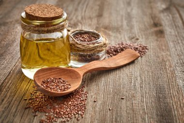 Keten tohumu ve ahşap bir masada bir şişe yağlı tahta kaşık. Sağlıklı yiyecek ve içecek konsepti. Uzayı kopyala Kapat.