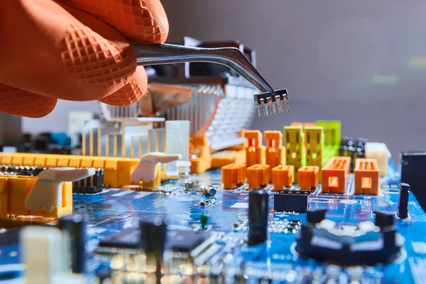 Mikroçipi cımbızla tutan ve elektronik ana kartı tamir eden adam..