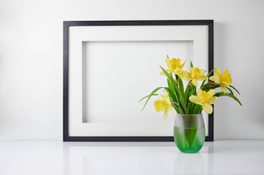 Ev iç mimarisi çiçek dekoru. Süslü çiçekleri beyaz masadaki vazoda çerçevelet. Arkaplanda narsisli bir poster.