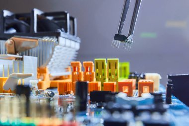 Mikroçipi cımbızla tutan ve elektronik ana kartı tamir eden adam..