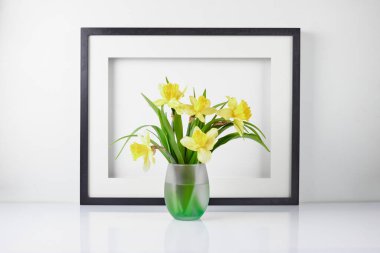 Ev iç mimarisi çiçek dekoru. Süslü çiçekleri beyaz masadaki vazoda çerçevelet. Arkaplanda narsisli bir poster.