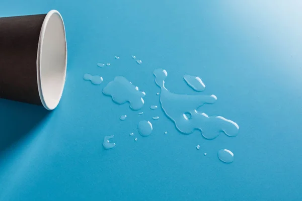 Dunkle Papiertasse Mit Abstrakten Tropfen Verschütteten Wassers Auf Blauem Hintergrund — Stockfoto