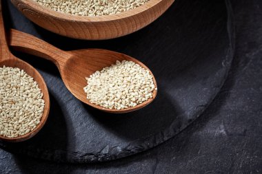 sesame seeds and a wooden spoon on a dark table. Black slateboard with wooden bowl. Copy space. Close up clipart