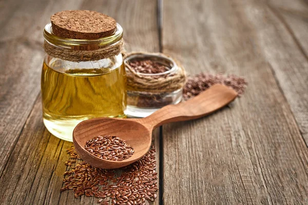 Keten tohumu ve ahşap bir masada bir şişe yağlı tahta kaşık. Sağlıklı yiyecek ve içecek konsepti. Uzayı kopyala Kapat.