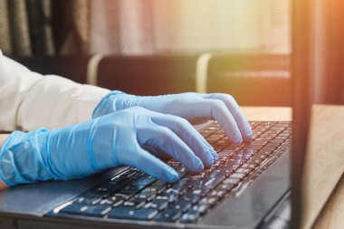 Laptop klavyesinde yazan koruyucu eldivenli bir kadın. Halka açık yerlerde Coronavirus covid-19 'dan koruma kavramı.