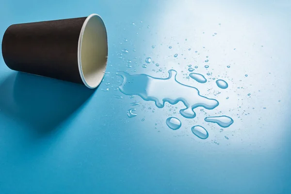 Dunkle Papiertasse Mit Abstrakten Tropfen Verschütteten Wassers Auf Blauem Hintergrund — Stockfoto