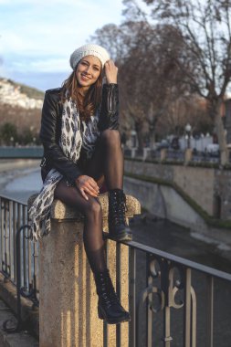 Güzel genç bir kadın oturmuş nehrin kenarında günbatımının tadını çıkarıyor.