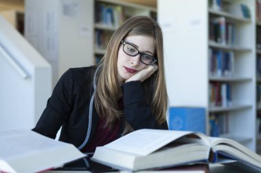 Genç bir kadın kütüphanede okuyor, sıkılmış, doymuş ve endişeli.