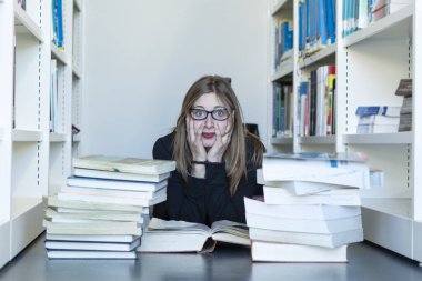 Genç kız öğrenci, kitapların arasında, kütüphanede ders çalışıyor.