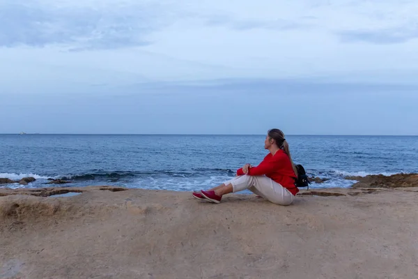 Una joven en Rock Seaside. Playa apedreada cerca del mar con cielo azul —  Fotos de Stock