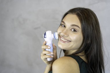 Young pretty woman doing skin care procedure. Cleaning face with machine copy space