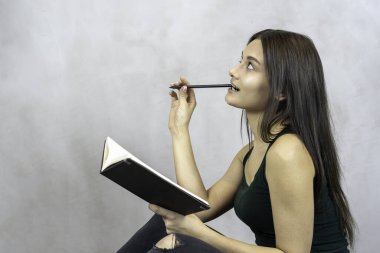 Genç, güzel bir kadın. Kalem ve not defteriyle. Gri arka planda gülümsüyor. Boşluğu kopyala