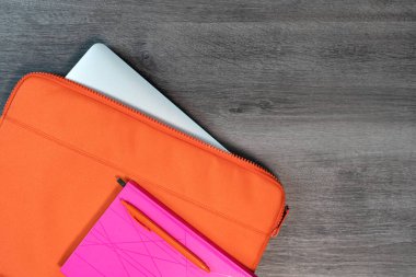 Pembe defter ve düz kalem içeren parlak turuncu dizüstü bilgisayar çantası.