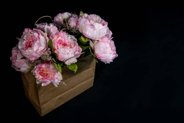 Siyah arka planda kağıt torba içinde pembe şakayık demeti