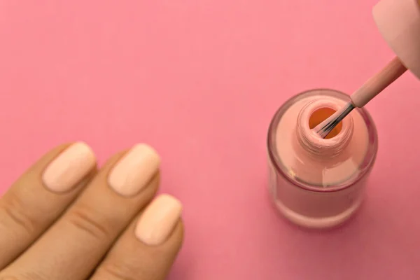 Pink nail polish with brush on pink background