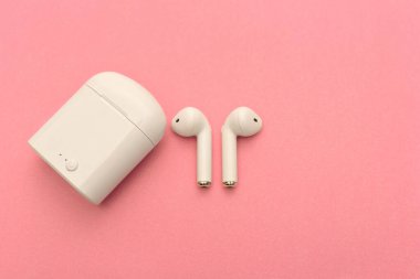 Kablosuz kulaklıklar ve pembe arka planda kablosuz şarj cihazı. Boşluğu Kopyala.