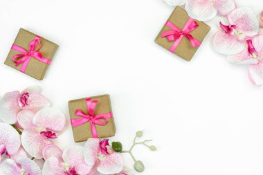 Beyaz arka planda pembe kurdeleli hediye kutuları ve orkide çiçekleri var. bahar konsepti. Boşluğu kopyala