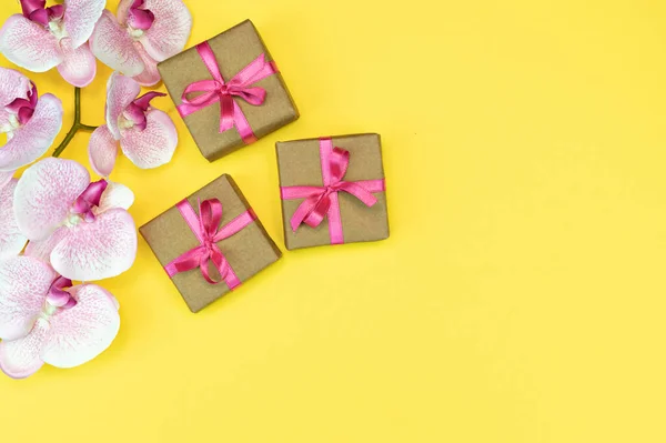 Flat-lay de presente caixas com fita rosa no fundo amarelo com flor de orquídea. conceito de primavera. Espaço de cópia — Fotografia de Stock
