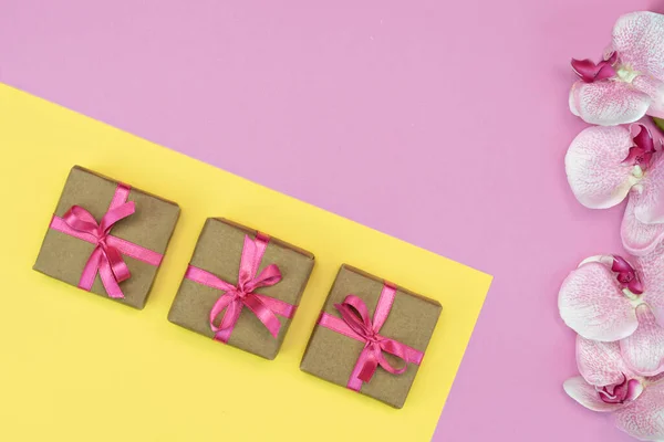 Flat-lay de presente caixas com fita rosa no fundo amarelo rosa com flor de orquídea. conceito de primavera. Espaço de cópia — Fotografia de Stock